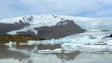 Obraz premium Melting icebergs floating in a glacier lagoon at the foot of an Icelandic glacier, surrounded by cold blue water and rugged mountains.