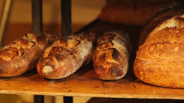 Skilled bakery worker arranges fragrant bread on shelves. Experienced worker uses wooden spatula designed for handling freshly baked bread