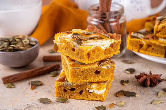 Sweet autumn baking recipe, pumpkin cream cheese brownies. Marbled pumpkin and cheesecake brownie bars on beige concrete background