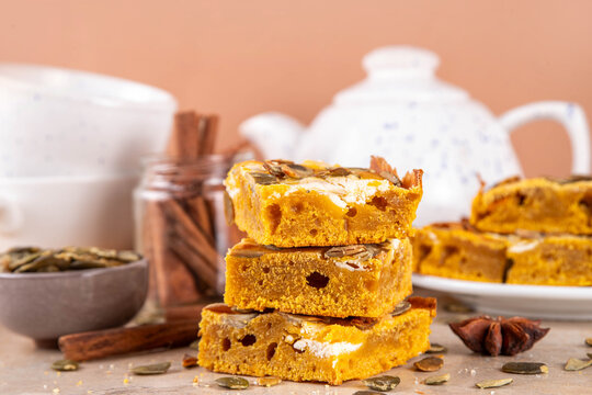 Sweet autumn baking recipe, pumpkin cream cheese brownies. Marbled pumpkin and cheesecake brownie bars on beige concrete background