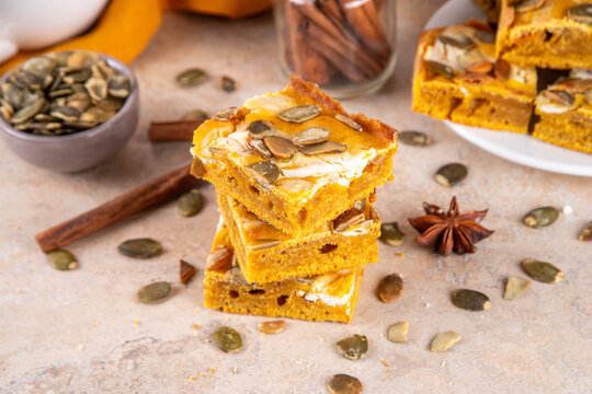 Sweet autumn baking recipe, pumpkin cream cheese brownies. Marbled pumpkin and cheesecake brownie bars on beige concrete background