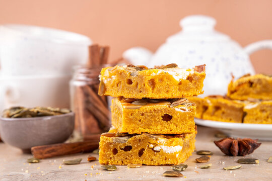 Sweet autumn baking recipe, pumpkin cream cheese brownies. Marbled pumpkin and cheesecake brownie bars on beige concrete background