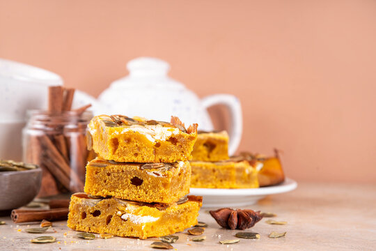 Sweet autumn baking recipe, pumpkin cream cheese brownies. Marbled pumpkin and cheesecake brownie bars on beige concrete background