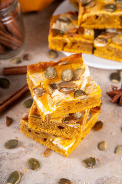 Sweet autumn baking recipe, pumpkin cream cheese brownies. Marbled pumpkin and cheesecake brownie bars on beige concrete background