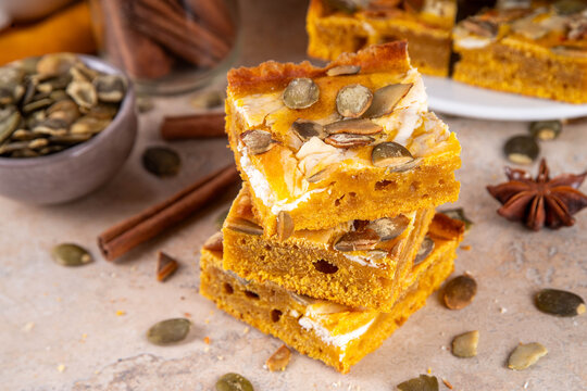 Sweet autumn baking recipe, pumpkin cream cheese brownies. Marbled pumpkin and cheesecake brownie bars on beige concrete background