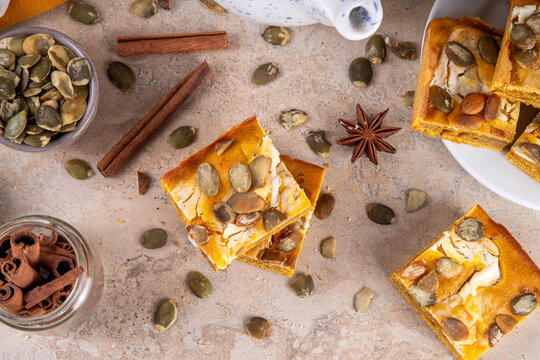 Sweet autumn baking recipe, pumpkin cream cheese brownies. Marbled pumpkin and cheesecake brownie bars on beige concrete background