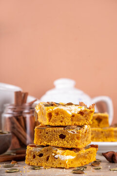 Sweet autumn baking recipe, pumpkin cream cheese brownies. Marbled pumpkin and cheesecake brownie bars on beige concrete background