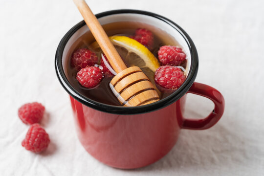 Raspberry tea with lemon and honey served in a red mug on a table, warm homemade beverage for cozy autumn and winter days