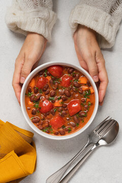 Hands holding a bowl of homemade bean stew with tomatoes on a light background, seasonal hearty comfort food and healthy vegetarian meal