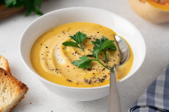 Creamy pumpkin soup with cream served in a bowl on a light kitchen table, homemade seasonal comfort food for cozy autumn and winter meals