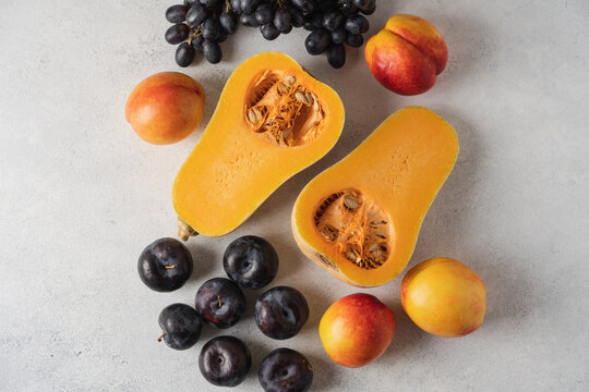 Autumn still life with butternut pumpkins, nectarines, plums and grapes on a light background, seasonal fresh fruits and vegetables harvest concept