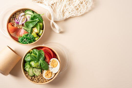 Healthy protein bowls with smoked salmon, egg, quinoa, avocado, spinach, cucumber and chuka seaweed salad in cardboard containers on a light beige background