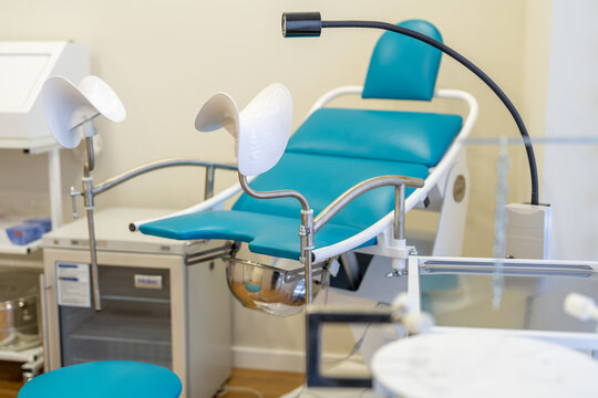 Interior of a modern, bright, and clean gynecological office featuring a teal examination chair equipped with stirrups.