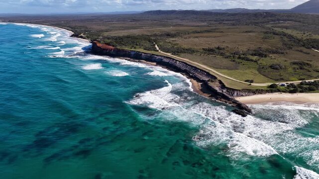 Aerial video flying over the rugged coastline at Lake Arragan, featuring sandy shoreline, rocky formations and waves rolling in from the Pacific Ocean