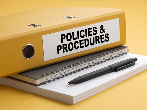 Yellow ring binder with policies and procedures label on top of notebooks and pen office supplies business documents corporate documentation black pen work desk