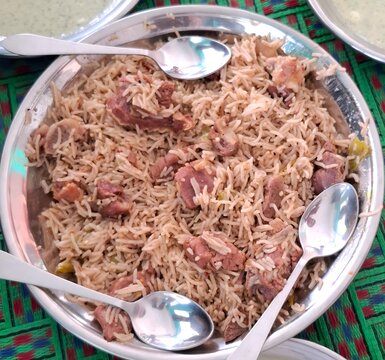 Traditional mutton pulao served in a metal platter with spoons