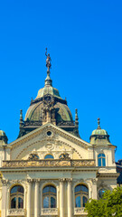 Fototapeta premium Building with statue under blue sky. The tall building features a statue on top against a clear blue sky. Sunlight shines on its detailed architecture.