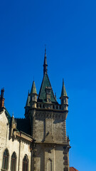 Historic castle tower under clear sky. A tall castle tower stands against a blue sky. The stone structure has pointed roofs. It is located in a historic area. © Daniil