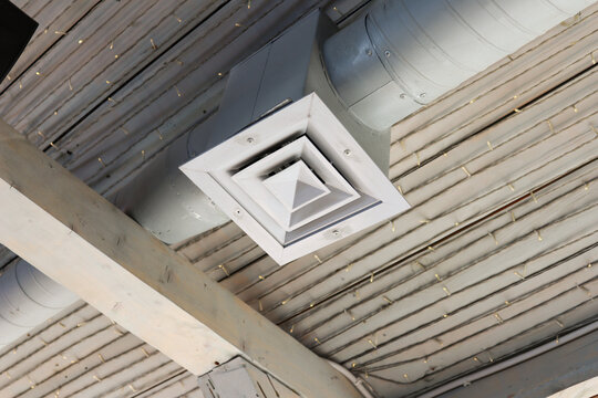 Close-up of a square HVAC air diffuser connected to exposed ventilation ducts on an industrial style ceiling. Building engineering detail representing air conditioning, ventilation, airflow, climate 