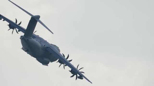 Heavy four engine military cargo plane, an Airbus A400M Atlas, performing a turning maneuver during a demonstration flight at an airshow