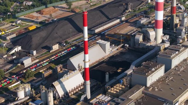 High angle view showing a large coal fired power plant. The industrial complex features prominent red and white smokestacks and a large coal pile