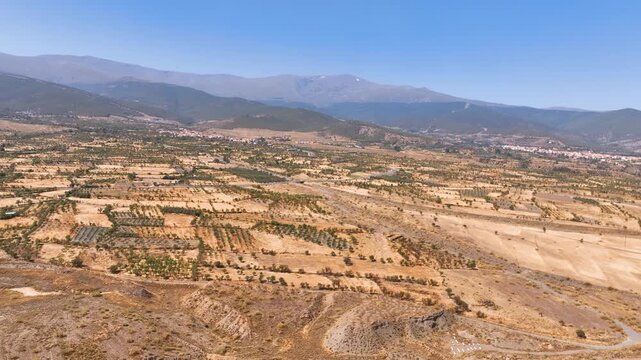 High flight above thinning orchards across the lowlands and foothills of Spain's famed Sierra Nevada mountain range towards villages, in mid Summer.