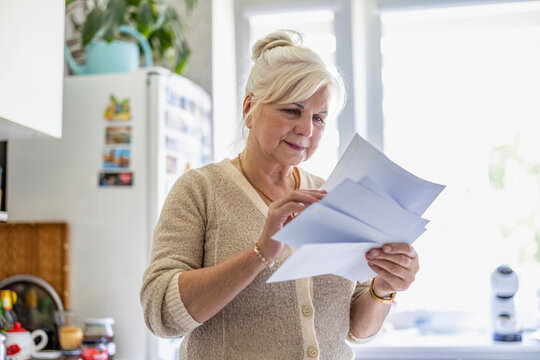 Senior woman reading her mail and documents in the kitchen
