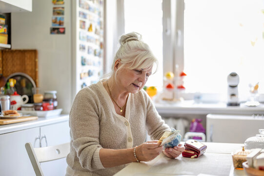 Senior woman counting money in her wallet at the kitchen table
