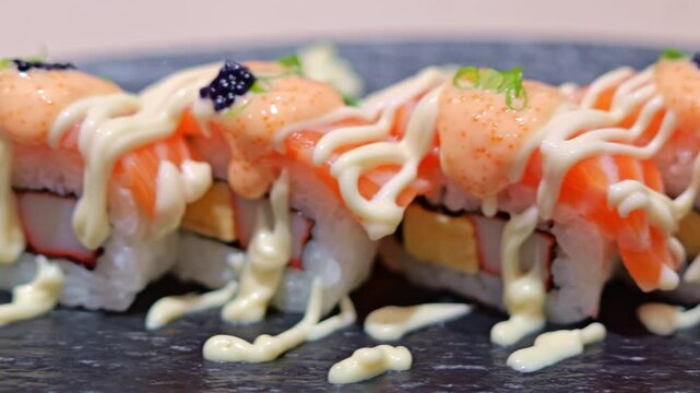 Japanese Salmon Sushi Roll with Creamy Spicy Sauce and Roe Garnish on Black Plate