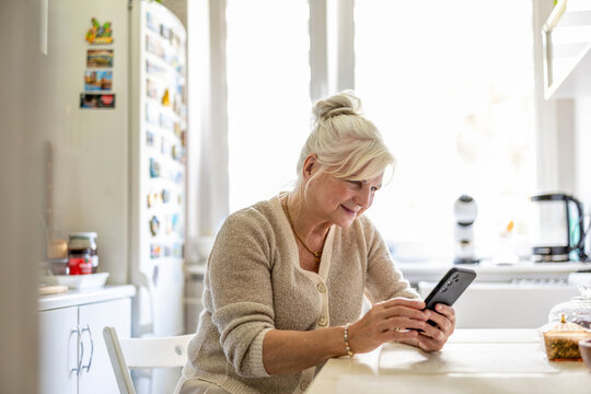Portrait of smiling senior woman using mobile phone in kitchen at home

