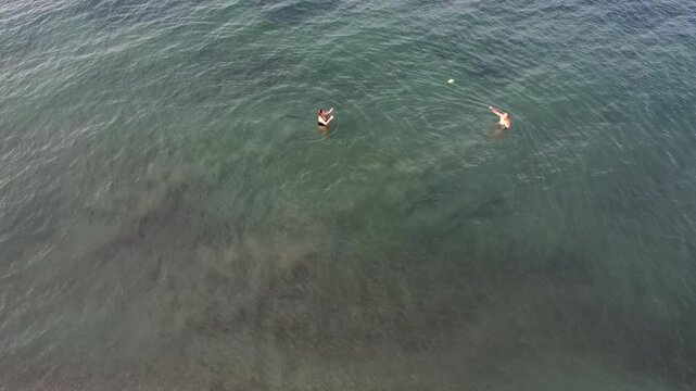 Drone aerial view of people having fun and playing with a ball in the sea near the beach of Alissos, Greece, capturing an energetic summer moment along the scenic Ionian coast
