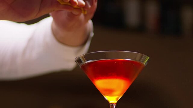 Extreme close up slow motion shot of a professional bartender squeezing a fresh lemon peel twist, expressing a fine mist of essential citrus oils over an elegant classic cocktail