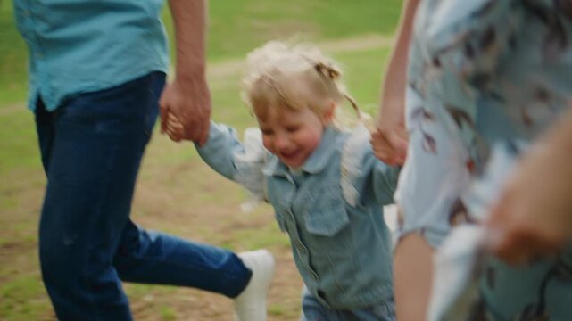 Young child laughs joyfully, held by two adults outdoors. Family moment captures playful, carefree energy. Perfect for themes like family bonding, childhood happiness, or outdoor adventures