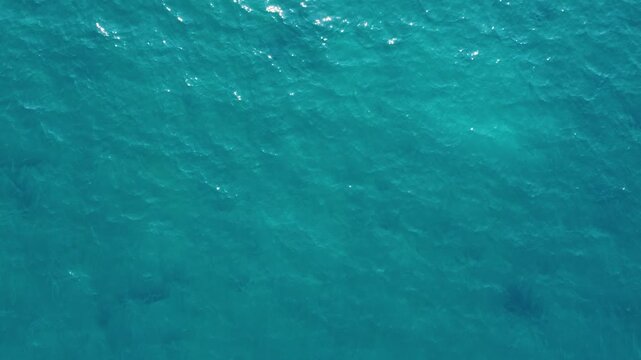 Top down drone view hovering above vibrant turquoise and deep blue ocean water with gentle surface waves reflecting sun rays in Cyprus.