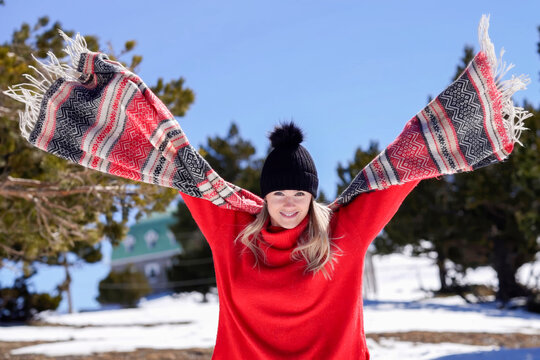 Happy woman in vivid clothing raises arms amidst snowcovered pine trees and clear sky