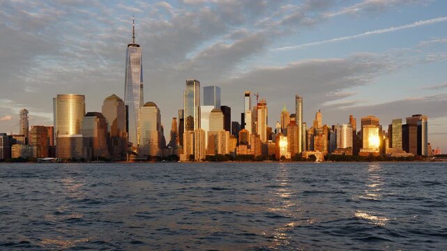 New York City Lower Manhattan skyline at sunset, with World Trade Center and Financial District skyscrapers in warm light across the Hudson River