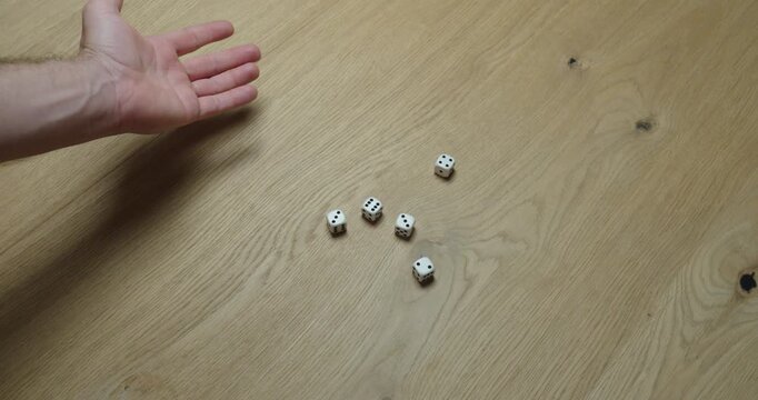 Close-up of a hand rolling multiple dice on a wooden table, representing luck, chance and gaming.