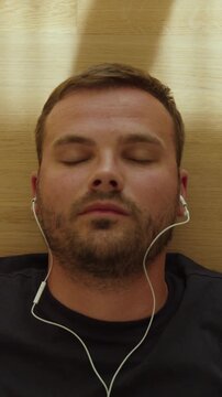 Close-up of a man lying down and putting earbuds into his ears to listen to music and relax.
