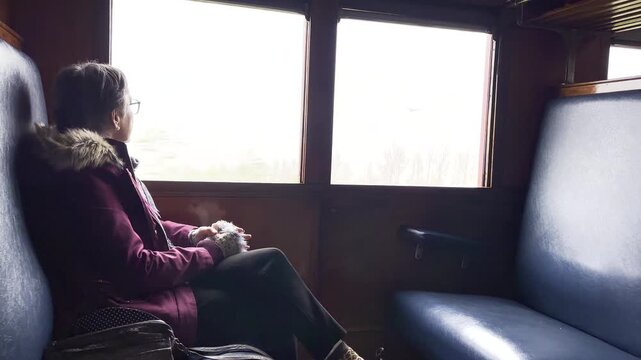 Female traveller on train journey stares out of window at passing countryside