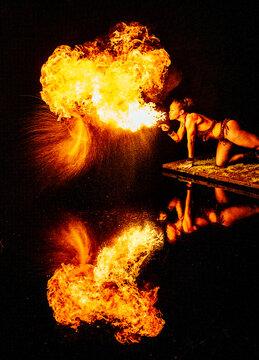 Fire breather performing at night with flames and reflection