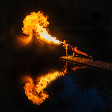 Fire breather performing on dock at night with flame reflection