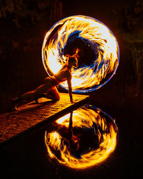 Fire African American dancer spinning flames on pier reflected