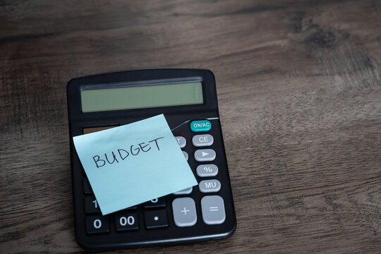 Blue sticky note with budget text stuck on black calculator on wooden desk