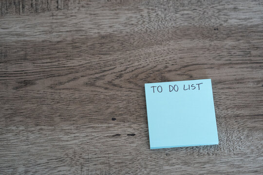 Blue sticky note pad with to do list text on dark wooden desk with copy space