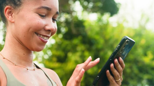 Joyful Black Woman with Natural Hair Using Smartphone Outdoors with a Happy Smile