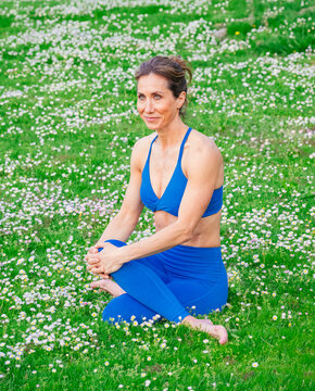 White woman practicing yoga outdoors on grassy field with flowers