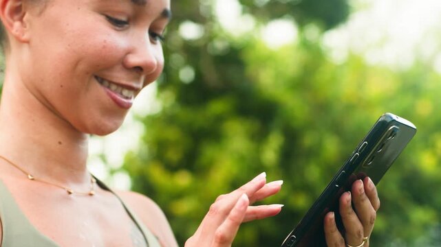 Happy Black Woman with Natural Hair Scrolling and Smiling on Her Smartphone Outdoors
