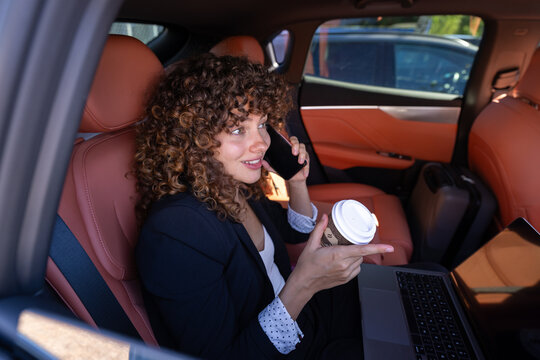 Businesswoman working remotely on laptop and phone inside car