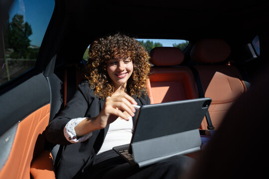 White woman using tablet for remote work in car back seat