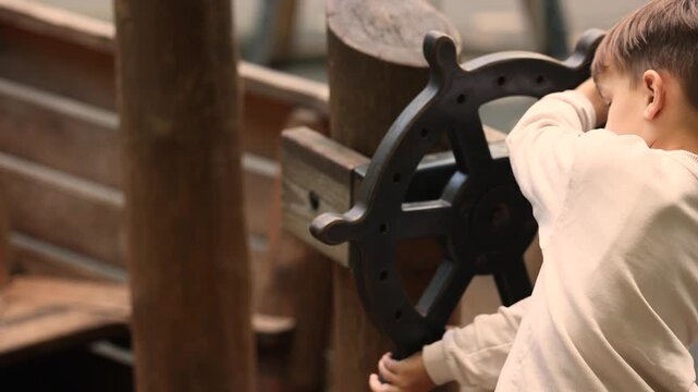Boy turns wooden ship wheel on playground pirate boat structure